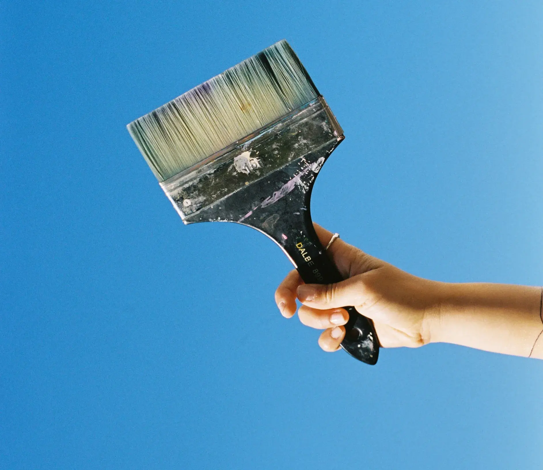 A hand holding a paintbrush against a blue sky