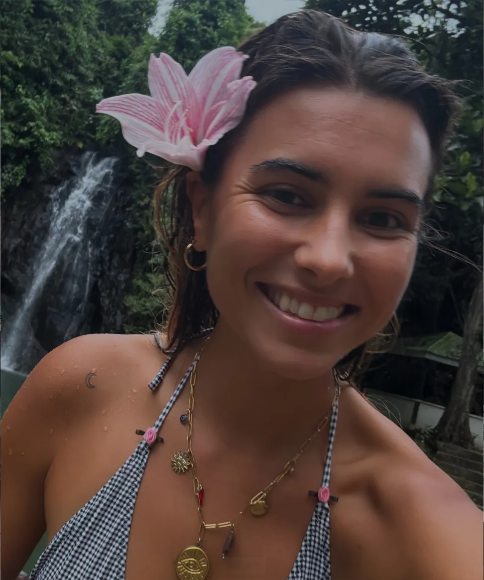 Ari smiling with a pink flower in her hair by a waterfall