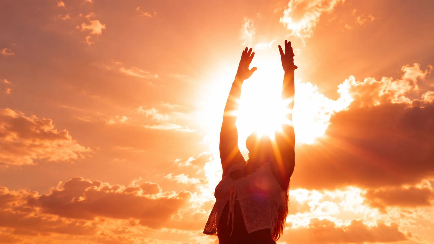 Woman reaching both arms toward the golden sun