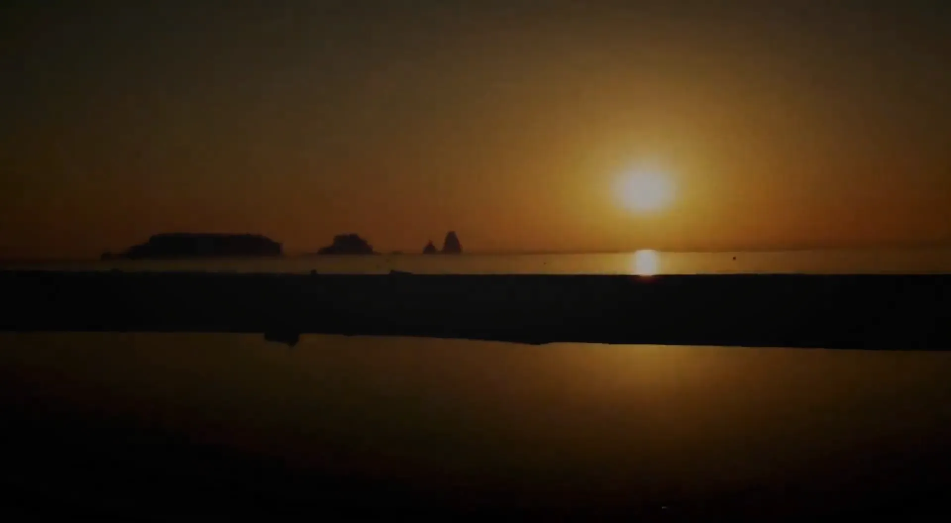 Sun setting over the sea behind rocky islands