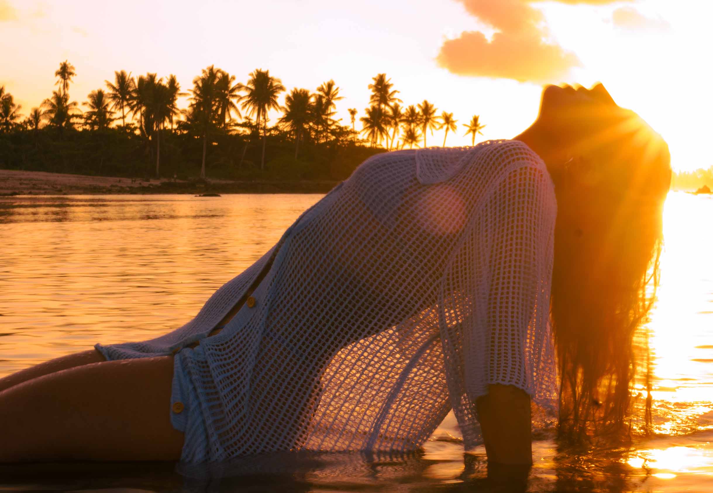 Ari arching back in the water at golden-hour sunset, palm trees behind